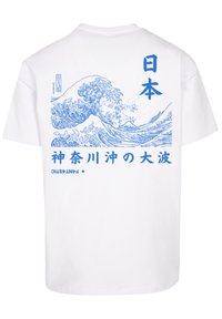 Bílý bavlněný tričko se modrou vlnou na grafice a japonským textem na zadní straně, ukazující složité linky a tučné písmo.