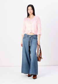 Light pink, knitted crop top with a scalloped hem and wide sleeves, paired with medium-wash, loose denim jeans and brown ankle boots.