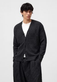 Mörkgrå stickad cardigan med knappframsida, ribbade manschetter och nederkant, i kombination med lösa svarta texturerade byxor. Enkelt design, mjuk textur.