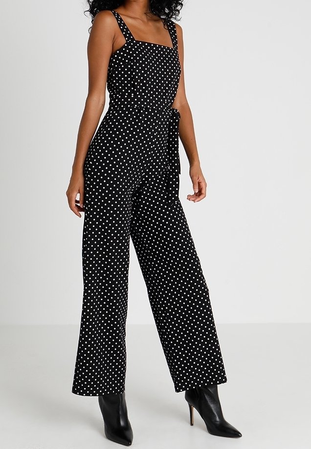 Svart prickig byxdress med fyrkantig halsringning, bred bendesign och midja med knytning. Tyget verkar lätt och har en jämn textur.