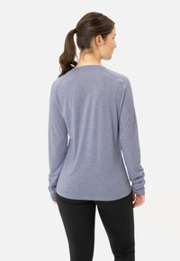 Langärmliges, leichtes Hemd aus meliertem blauen Stoff mit relaxed Fit und gerippten Bündchen. Getragen mit schwarzen Leggings, Rückansicht gezeigt.