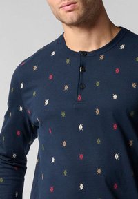 Camicia a maniche lunghe blu navy realizzata in tessuto morbido, con collo henley a bottoni e un motivo a rombi colorato in rosso, verde e beige.