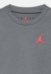 Γκρι βαμβακερό μπλουζάκι με στρογγυλή λαιμόκοψη, που διαθέτει κόκκινο κεντημένο λογότυπο Jumpman στο στήθος. Μαλακή υφή, casual σχεδιασμός.