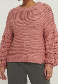 Stickad rosa tröja med texturerad kropp och mönstrade, puffy ärmar. Har rund halsringning och ribbad nederkant. Mjuk, tjock garn.