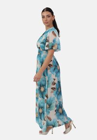 Maxiklänning i lätt tyg med stora blå blommönster, elastisk midja, korta puffärmar och en flödande silhuett.