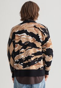Stickad tröja med ett abstrakt mönster i beige, svart och vitt, med ribbade avslut och ärmslut. Designad med en klassisk krage.