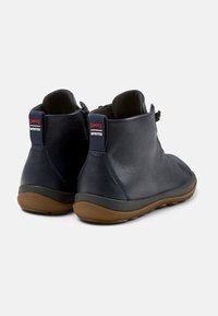 Botines de cuero azul marino con una superficie texturizada, que presentan un cierre de cremallera y un sutil logo rojo, montados sobre una suela de goma.