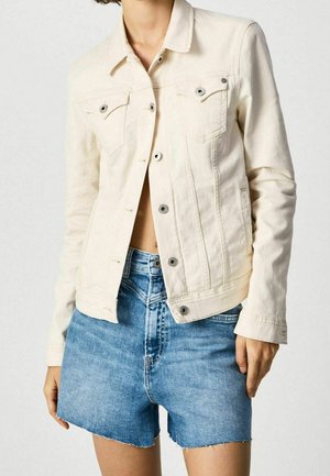 Vrouw draagt een beige denimjack met knopen, gecombineerd met een high-waisted blauwe denimshort met rafelige zomen.