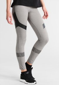 Leggings gris clair avec des accents géométriques et des rayures noires, fabriqués dans un tissu extensible, avec un design ajusté et une longueur jusqu'à la cheville.