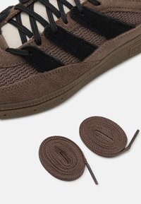 Sneaker in tessuto marrone con accenti in tessuto nero, superficie texturizzata e lacci neri piatti. Include due lacci in stile corda marroni.