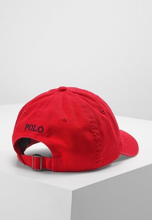 Rød Polo baseballkasket med justerbar strop og metalspænde, hvilende på en hvid overflade set bagfra.