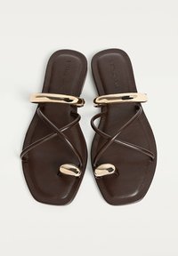 Ruskeat litteät sandaalit ristiin menevillä hihnoilla, kultaisilla metallikoristeilla, neliön muotoisella kärjellä ja sileällä nahkapinnalla.