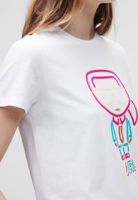 Camiseta blanca de algodón con un gráfico colorido de un personaje con cabello rosa, gafas de sol y un traje verde.