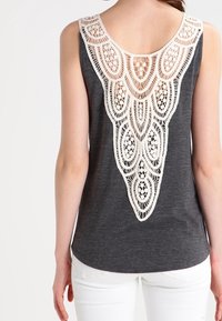 Grå linne med en bred, vit spetsdetalj på ryggen med intrikata blommönster; mjukt tyg med avslappnad passform och rundad fåll.