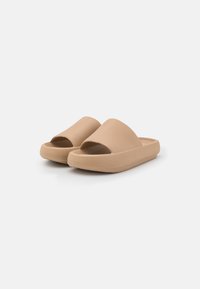 Beige Slipper-Sandalen mit einer strukturierten Oberseite und offenem Zehenbereich. Sie verfügen über eine dicke Gummisohle und eine glatte Oberfläche für zusätzlichen Komfort.