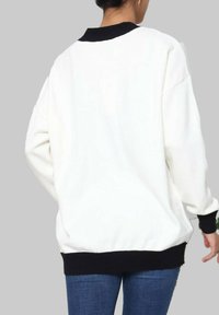 Sweatshirt blanc avec col et poignets côtelés noirs, affichant une coupe ample et une texture douce, assorti avec un jean bleu.