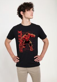 Svart bomullströja med ett grafiskt tryck av en muskulös karaktär i röd och svart, med texten "RED HULK" bredvid. Kortsleeves, rund hals.
