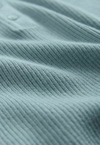 Tessuto azzurro chiaro a coste con un motivo testurizzato, caratterizzato da piccoli bottoni. Il materiale sembra morbido e leggermente elastico.