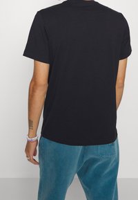 Černé bavlněné tričko s krátkým rukávem, kulatým výstřihem a volným střihem, v kombinaci s světle modrými tepláky s zadní kapsou.