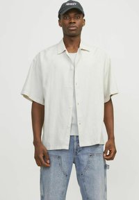 Lys, kortærmet skjorte med knapper i en cremet farve med en afslappet pasform; bæres over en grå ribbet tanktop og parret med lyseblå jeans.