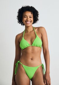 Lys grønn bikini med teksturert stoff, trekantet topp med justerbare stropper og knytedesign i bunnene med gullakenter.
