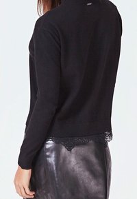 Suéter negro de cuello alto con dobladillo de encaje, combinado con una falda de cuero negra brillante con un patrón acolchado.
