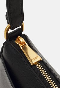 Coin d'un sac à main en cuir noir avec une fermeture éclair en or et des accents en métal. Le tirette de la fermeture éclair est bien en vue avec une marque gravée.
