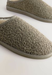 Graue Slipper zum Hineinschlüpfen mit einem Obermaterial aus strukturiertem Stoff, weichem Innenfutter und einer soliden Gummisohle. Die Ränder sind mit einem kontrastierenden Besatz veredelt.