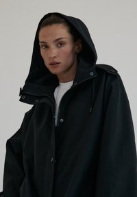 Czarna, oversize kurtka z zamkiem błyskawicznym z przodu, kapturem i zatrzaskami. Wykonana z gładkiego materiału o minimalistycznym designie.