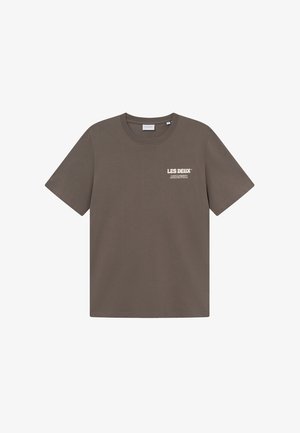 Smeđa pamučna majica s okruglim izrezom, kratkim rukavima i malim bijelim logom na lijevoj strani prsnog koša. Glatka tekstura, ležeran kroj.