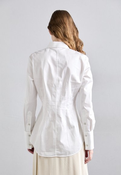 Bílá ko shirt s dlouhým rukávem, slim fit, s zádovým přešitím, zapínáním na knoflíky na manžetách a zakřiveným lemem. Vyrobena z hladké, texturované látky.