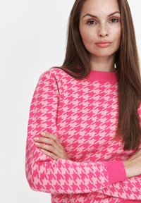 Różowy sweter w wzór houndstooth z okrągłym dekoltem i ściągaczami. Charakteryzuje się teksturowanym wzorem w różnych odcieniach różu.
