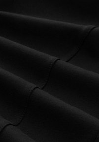 Zwarte stof met een gladde textuur, met meerdere plooien en naden, die een zachte, gedrapeerde vorm illustreert. Geen zichtbare patronen of accenten.