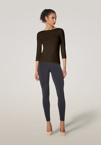 Langarm-Braun Oberteil mit U-Boot-Ausschnitt, kombiniert mit anthrazitfarbenen Leggings und hellrosa High Heels. Glattes Material mit figurbetontem Design.