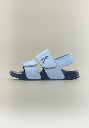 Σανδάλι Calvin Klein σε ανοιχτό γαλάζιο με δύο ρυθμιζόμενους ιμάντες και σκούρο μπλε υφασμάτινη σόλα σε ουδέτερο φόντο.