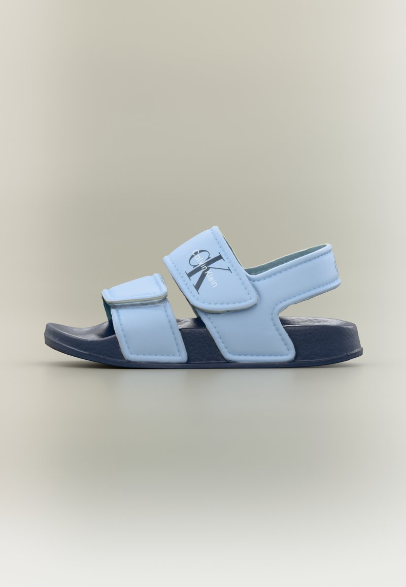 Σανδάλι Calvin Klein σε ανοιχτό γαλάζιο με δύο ρυθμιζόμενους ιμάντες και σκούρο μπλε υφασμάτινη σόλα σε ουδέτερο φόντο.