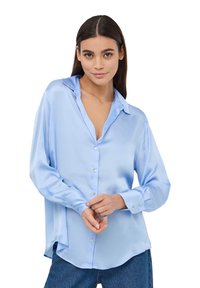 Camicia button-down in satin blu chiaro con colletto, maniche lunghe e spacchi laterali, abbinata a jeans in denim blu.
