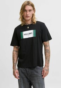 Schwarzes T-Shirt mit einem grünen und weißen rechteckigen Logo mit dem Text "JACK & JONES", aus weichem Stoff mit kurzen Ärmeln. Lässiger Schnitt.