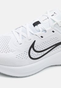 Hvide sportssko med åndbart mesh-overdel, sort swoosh-logo, tekstureret mønster og hvide snørebånd. Har en polstret sål.