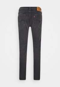Jean noir slim avec deux poches arrière, une étiquette de marque en cuir sur la ceinture, et une petite étiquette rouge sur la poche droite.