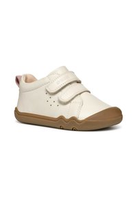 Zapato de cuero blanco con dos correas de Velcro, suela de goma marrón claro y un acento de tela rosa en el talón. Cuenta con perforaciones para transpirabilidad.