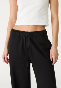 Pantalons de survêtement noirs en tissu doux, dotés d'une taille élastique avec cordon de serrage et de poches latérales. Design minimaliste avec une coupe décontractée.