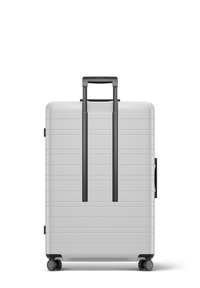 Silver hard-shell suitcase with textured surface, two black retractable handles, spinner wheels, and side grip. Vertical grooves accent the design.