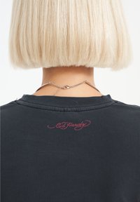 Černé bavlněné tričko s kulatým výstřihem a červeným vyšívaným logem "Ed Hardy" na zadní straně. Úzký střih s krátkými rukávy.