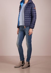 Námořnická prošívaná bunda s modrou podšívkou, žebrovaný světle modrý svetr, úzké modré džíny a šedé kotníkové boty s černými akcenty.