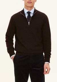 Dunkelbrauner Zip-Neck-Pullover aus weichem Material, figurbetonter Schnitt mit gerippten Bündchen, kombiniert mit einer navy Cordhose und einem hellblauen Hemd.