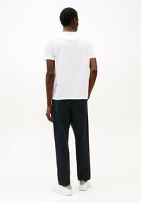 White short-sleeve T-shirt, paired with dark navy tapered pants, displayed from the back. The shoes are white with grey accents.