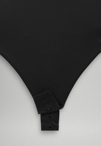 Crni bodysuit napravljen od glatkog materijala s V-oblikom. Ima dva dugmeta s kopčama na dnu, minimalistički stil bez uzoraka.