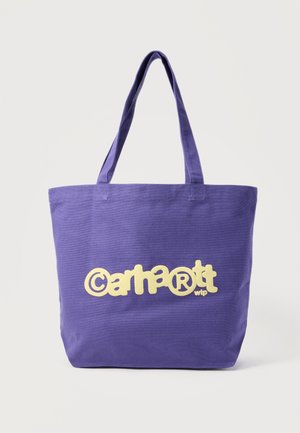 Lila vászontáska hosszú fogantyúkkal, a sárga "Carhartt WIP" logó középen elöl látható.