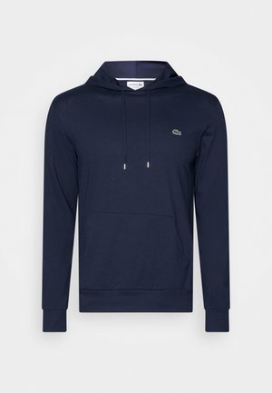 Granatowa bluza z kapturem wykonana z miękkiego materiału, z przednią kieszenią i małym zielonym logo na piersi.